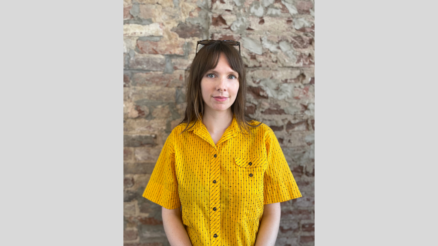 Nina Peterson standing in front of a brick wall wearing a yellow blouse.
