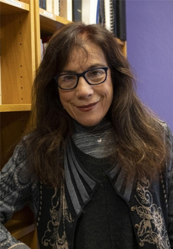 Amelia María de la Luz Montes smiling and standing in front of wooden bookshelf