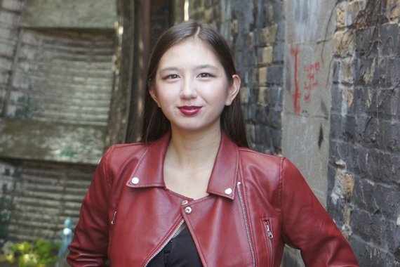 Corrine Olson in a red leather jacket, standing in front of a wall of bricks. 