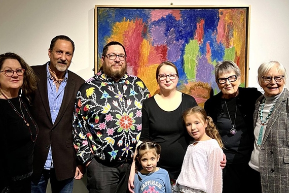 A multigenerational family stand in front of a colorful abstract painting