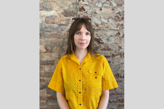 Nina Peterson standing in front of a brick wall wearing a yellow blouse.