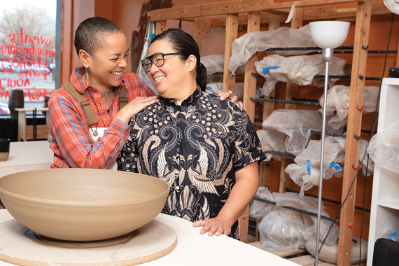 Two women embrace and smile inside a ceramics studio