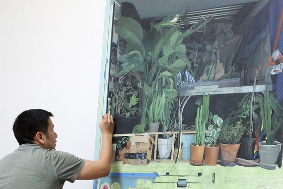 An artist works on a large painting of potted plants in the back of a moving truck