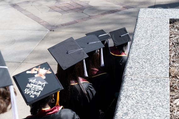 A picture taken from behind of students wearing graduation robs and cap walk down the stairs on campus.