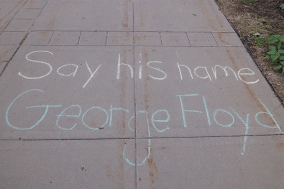 A photo of the phase "Say His Name George Floyd" written in chalk on a sidewalk