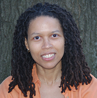 Head and shoulders photo of poet Evie Shockley in orange shirt against tree trunk background