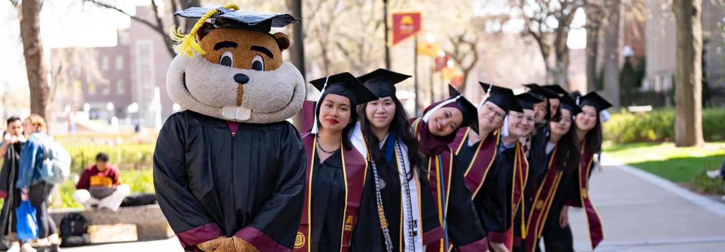 Goldy Gopher and several graduates stand in a line on Northrop Mall