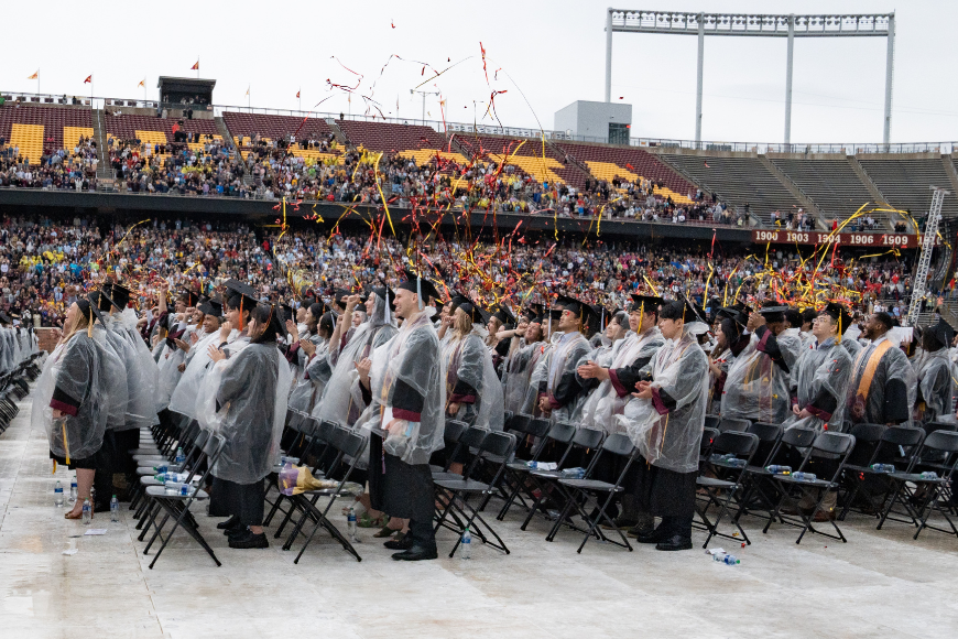 CLA undergrads clad in regalia and ponchos stand and throw streamers to celebrate