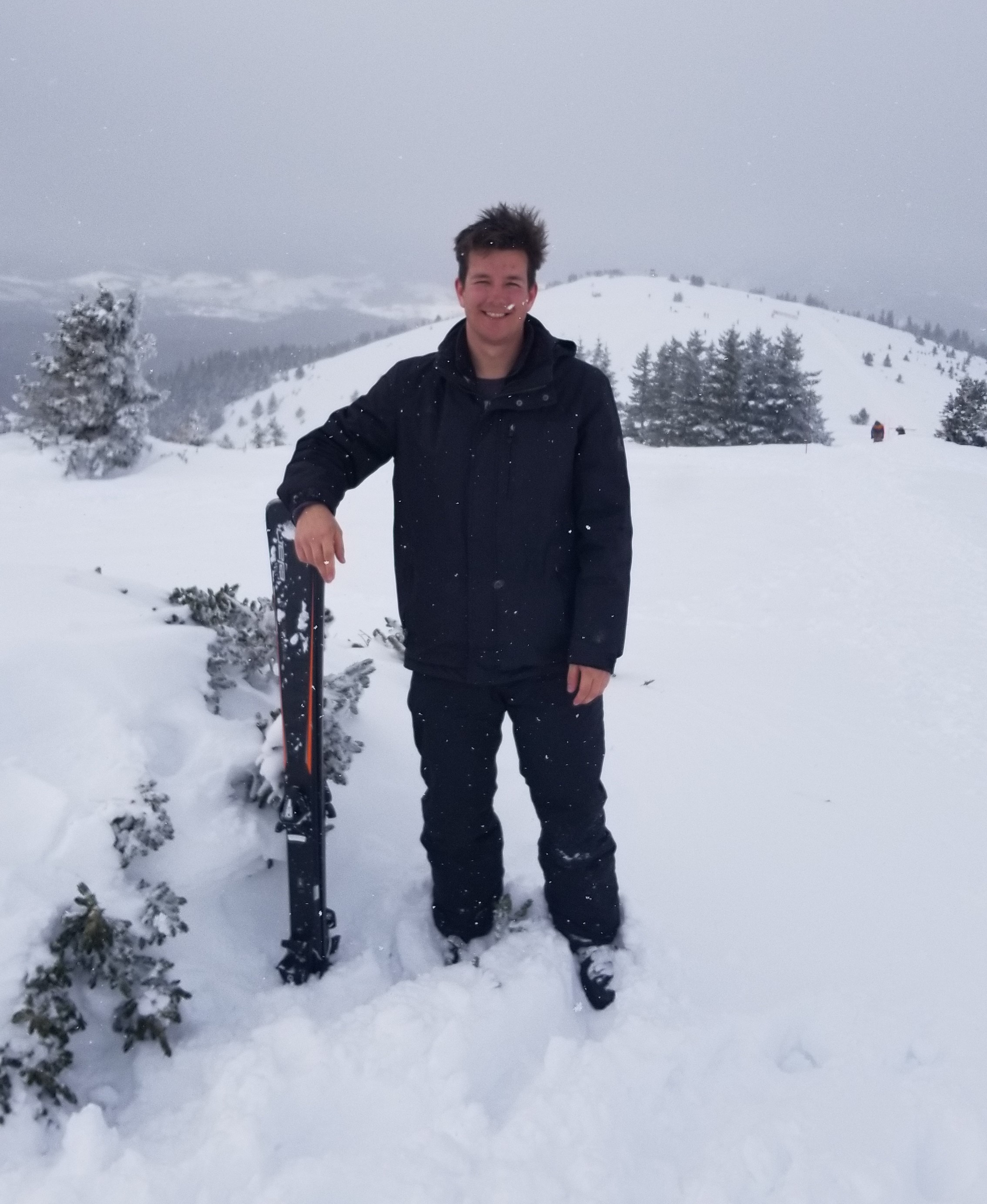 Elias poses next to his skis on a snowy hill in Colorado