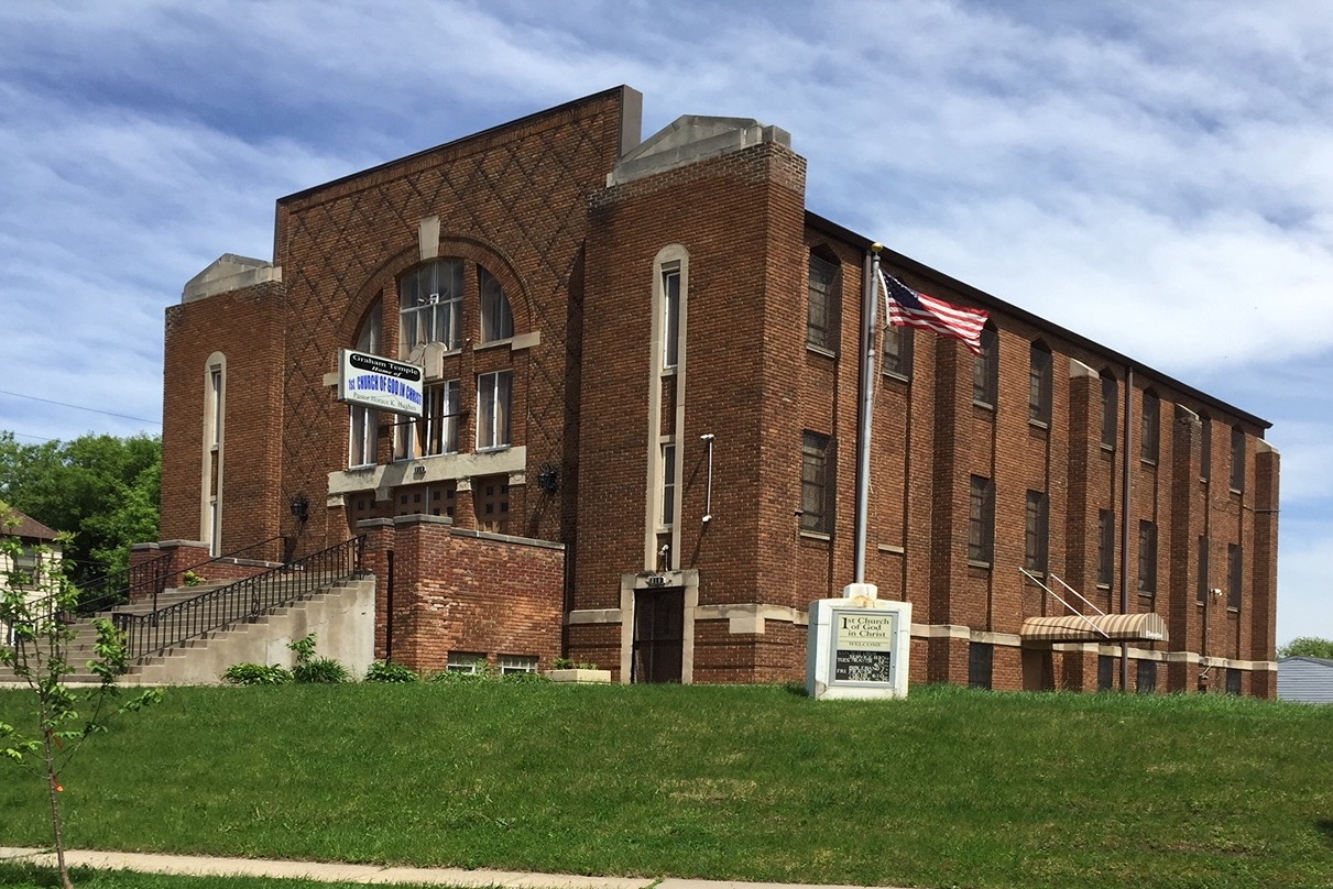 exterior of First Church of God in Christ building in front of a blue sky; a large, brick building surrounded by grassy space, two stories of narrow windows, and front semi-circular window design