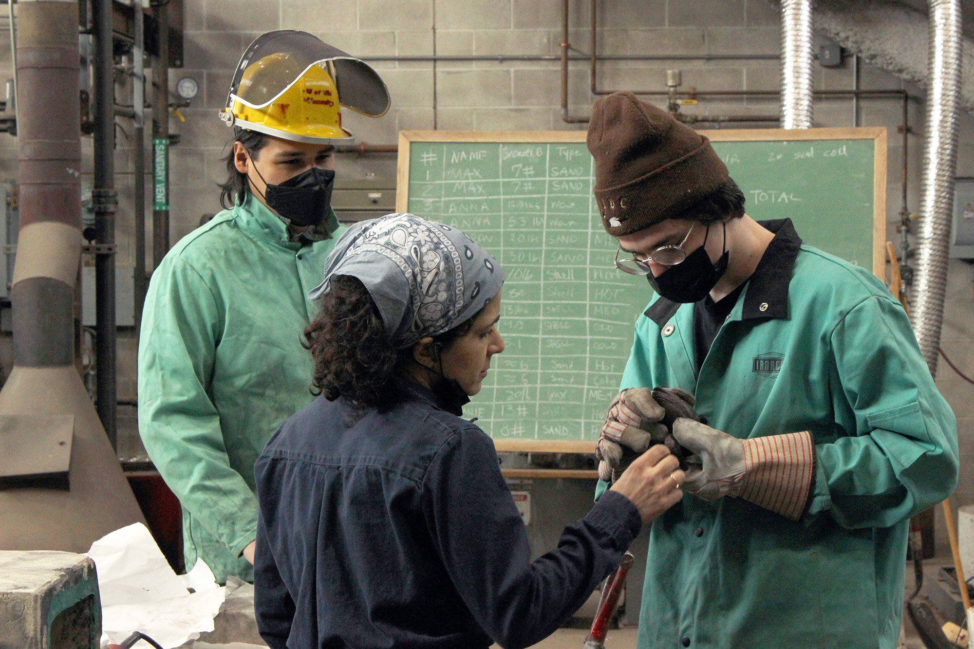Assistant Professor Rotem Tamir inspects a student's bronze work while another looks on