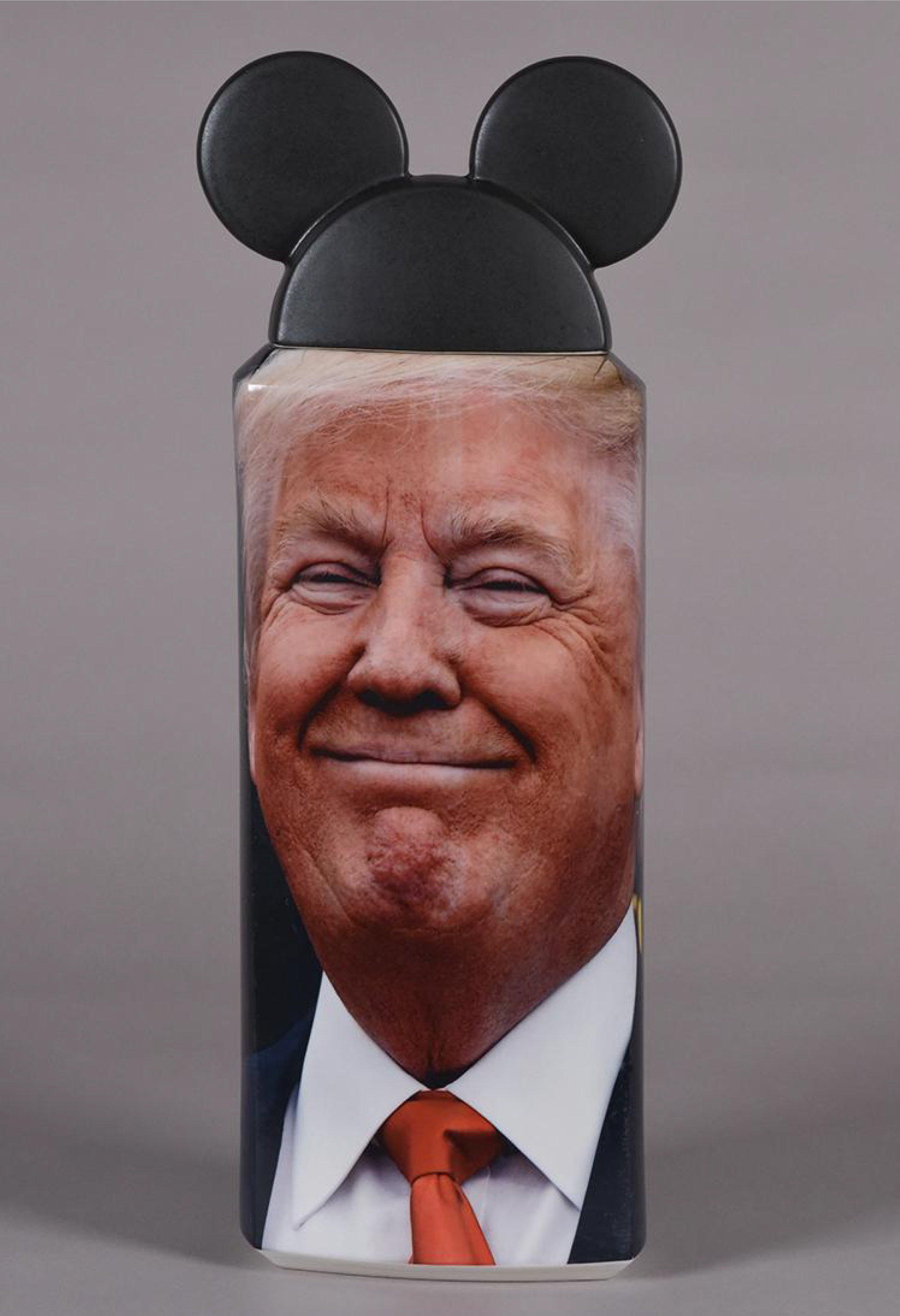 Lidded ceramic vessel with a photographic image of Donald Trump. The vessel's lid is made to look like Mickey Mouse ears