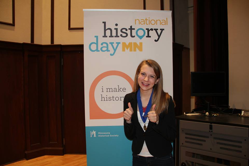 Maddie Love poses in front of a National History Day MN sign.