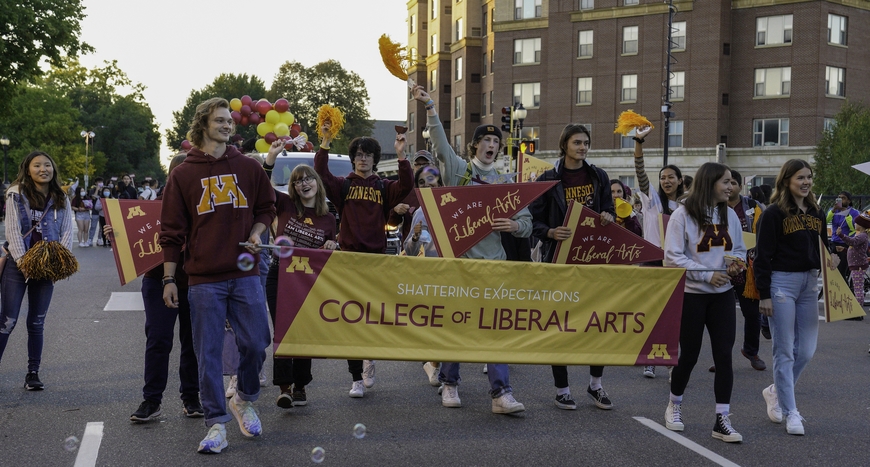 Students walking in parade and holding a banner that says College of Liberal Arts