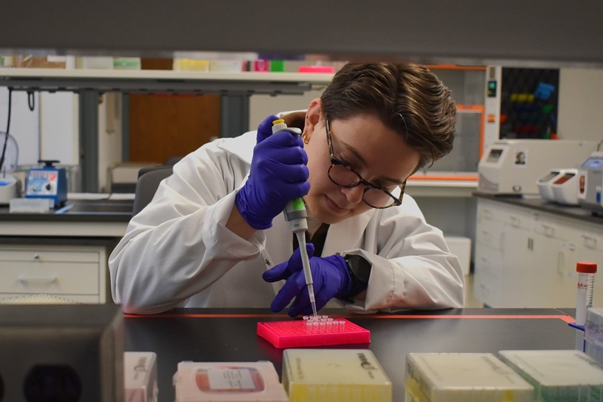 PhD candidate Laura Pott in a lab coat and gloves, using a pipette in a lab.