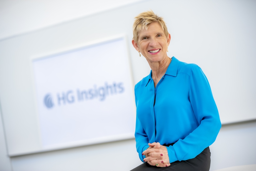 Elizabeth Cholawsky wears a bright blue button down shirt and poses in front of her company's logo HG Insights