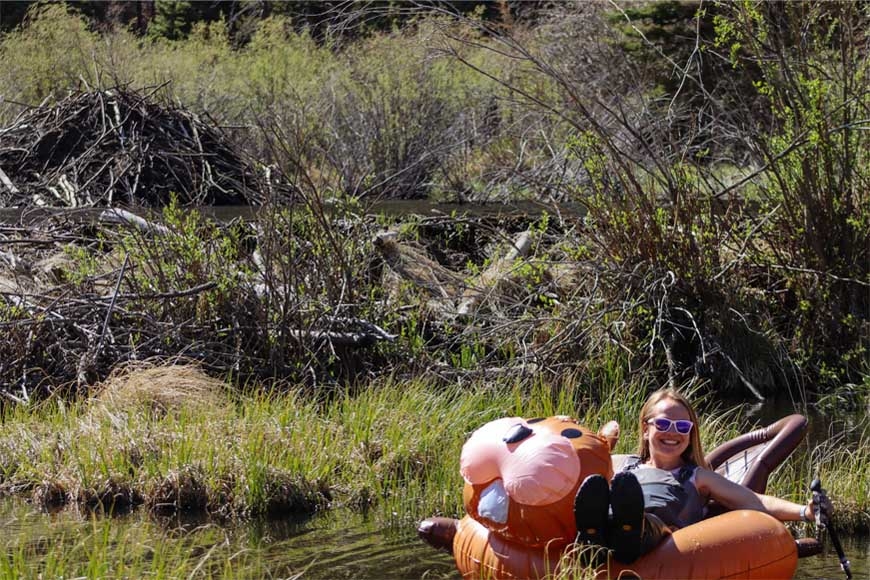 Emily Fairfax, a white woman wearing sunglasses, sits on a beaver pool floatie in an outdoors body of water