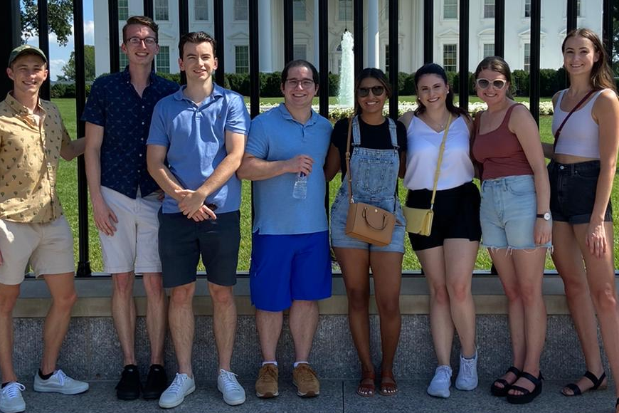 A group of 8 students posing in front of the White House. They are participants in the Kissinger Summer Academy.