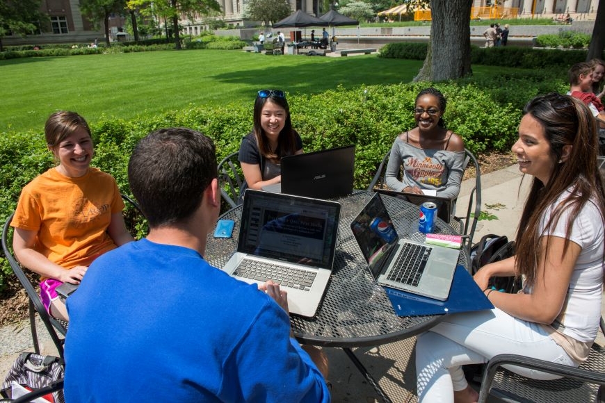 A group of students with laptops sitting at a table outside on Northrop Mall.