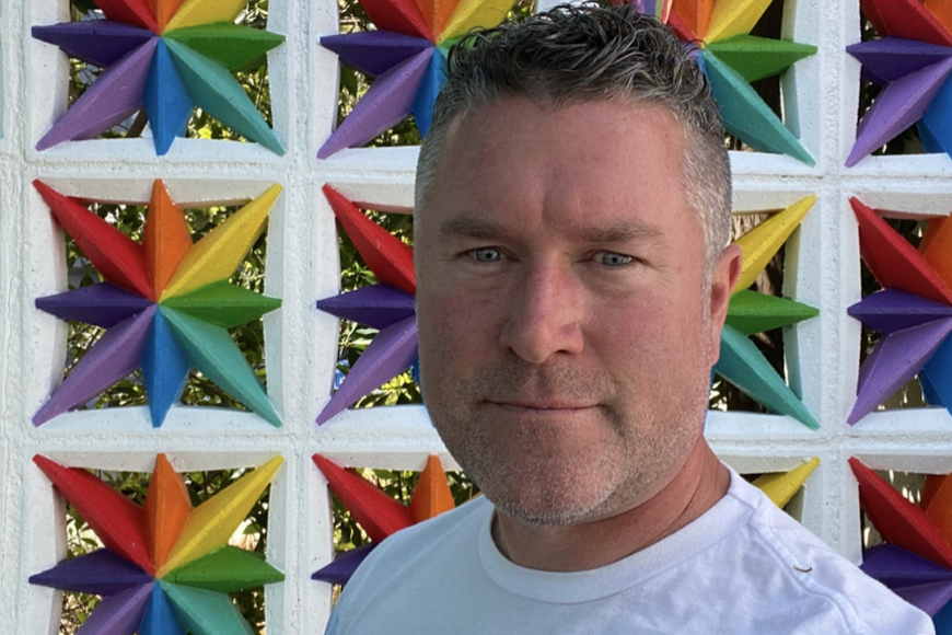 Tony Biel in front of a wall with rainbow decorations.