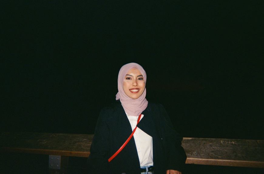 Yasmeen Iman Junaidi Jaafar wearing a light purple hijab and a black coat, standing outside at night