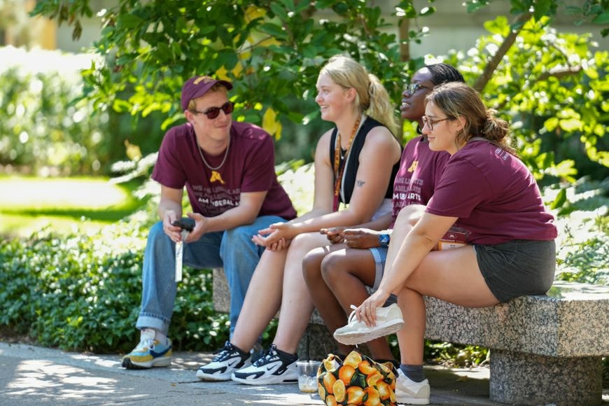 Four CLA students sitting on a bench, engaged in conversation outside.