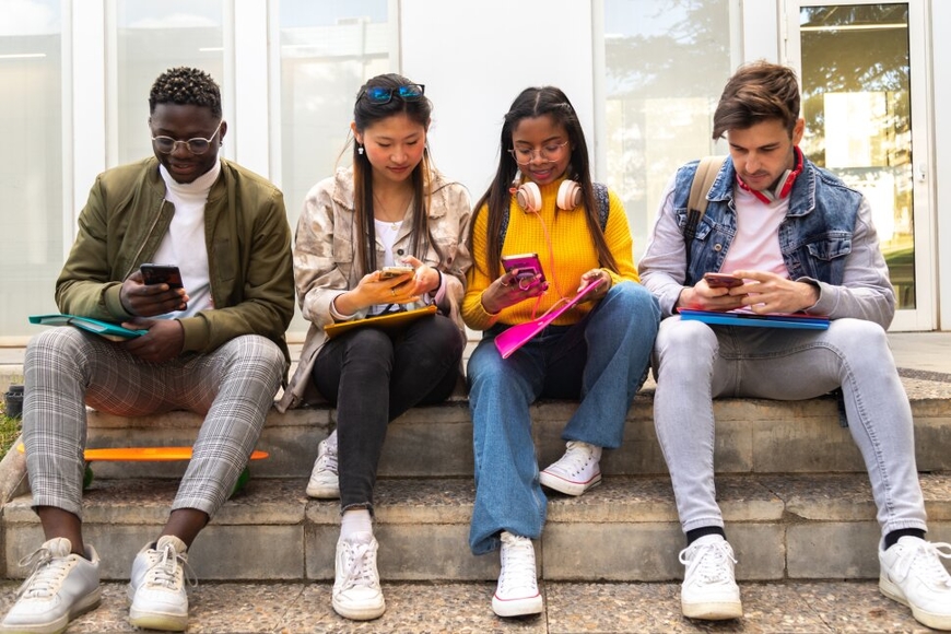 Four young adults sitting on a step and looking at their phones