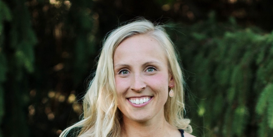 blond woman smiling at camera in front of green bushes