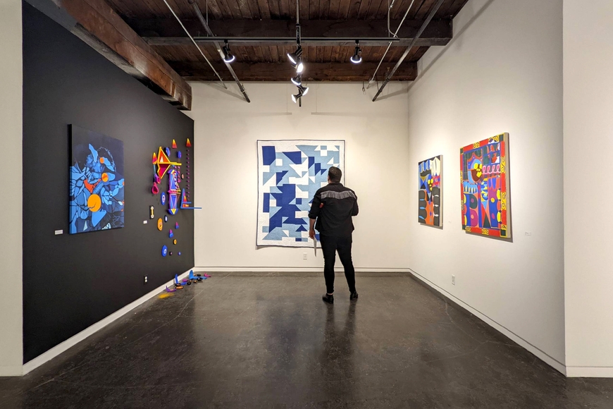 Installation view of artwork in Black Abstraction in the Midwest at SooVAC, with a person standing in front of a large blue and white quilt