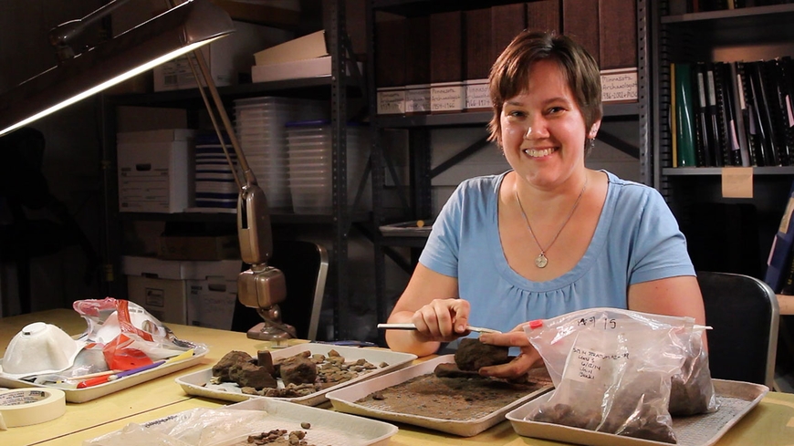 Amy Selvius is an undergrad archaeology intern. She is in a lab working with some tools and materials.