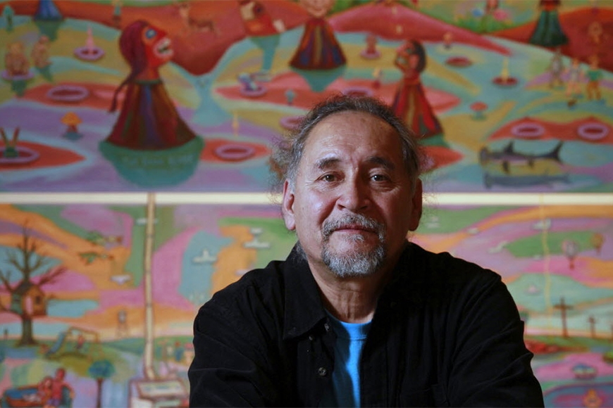 Portrait: Jim Denomie sits in front of some of his colorful paintings