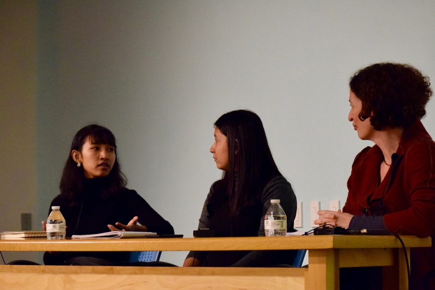 Three women, one with short dark hair in a black top, one with long black hair also in black, and the last with short auburn and curly hair, sit at a desk looking at one another in discussion.