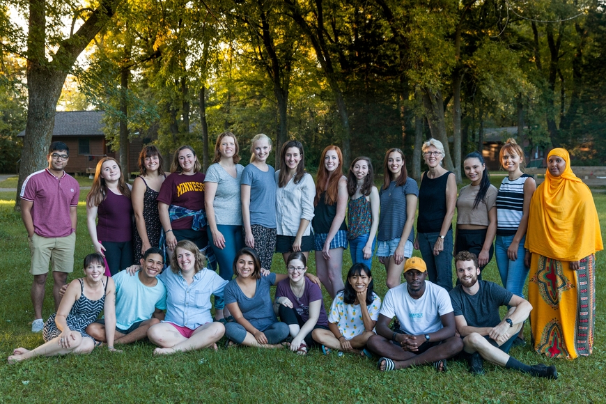 large group of diverse students posing in front of a background of trees and bushes in casual clothing