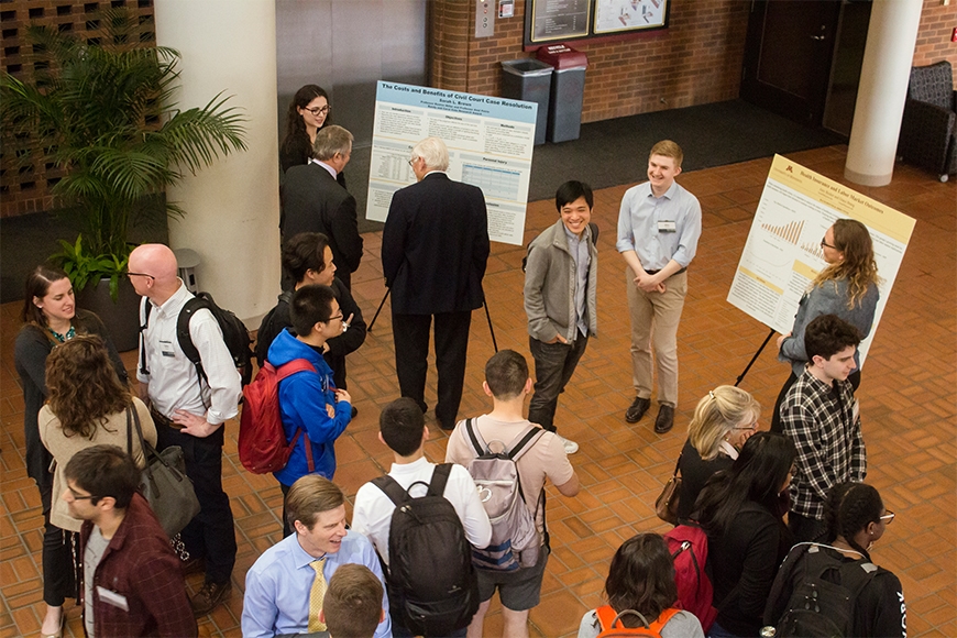A group of people walking around and observing poster boards at a poster session