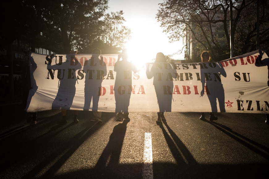 line of people holding a protest banner, back lit by the sun