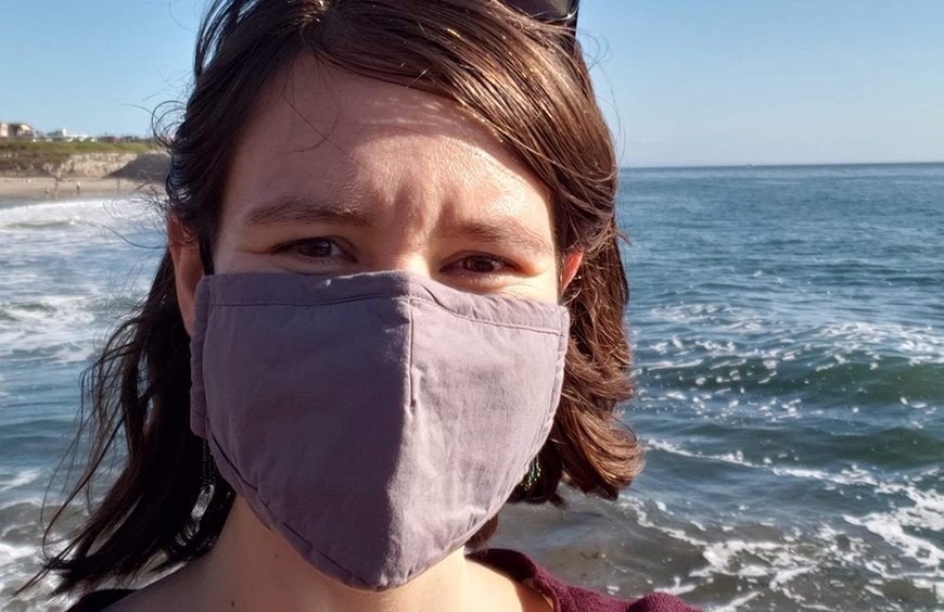 Photo of PhD candidate Zoe Rodine head with mask covering lower face in front of ocean