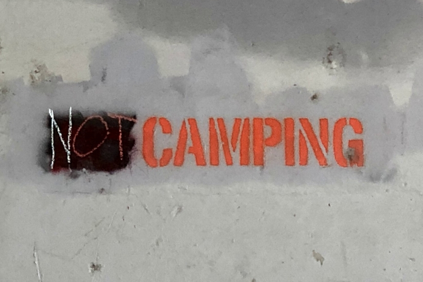 Concrete wall with graffiti that reads "Not Camping"