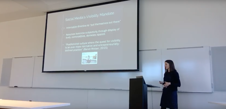 Image shows Dr. Duffy standing in front of her presentation, looking down at her notes. 