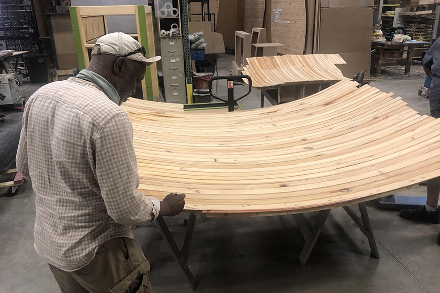 Photo showing back of man tracing line on curved piece of wood composed of thin strips