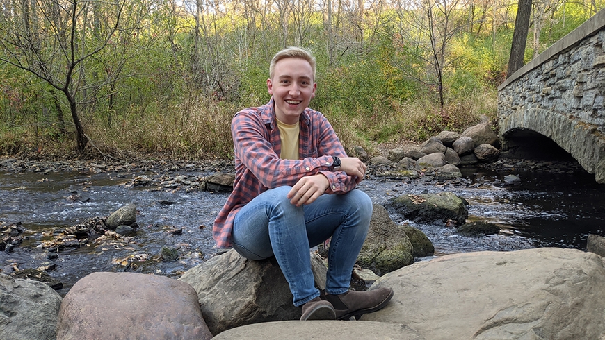 Photo of English major Ethan Voss sitting on rocks by river