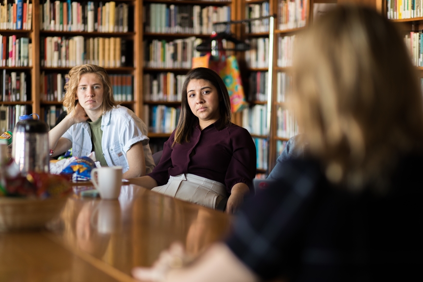Three female students sitting in a library two facing the camera and one facing the other two