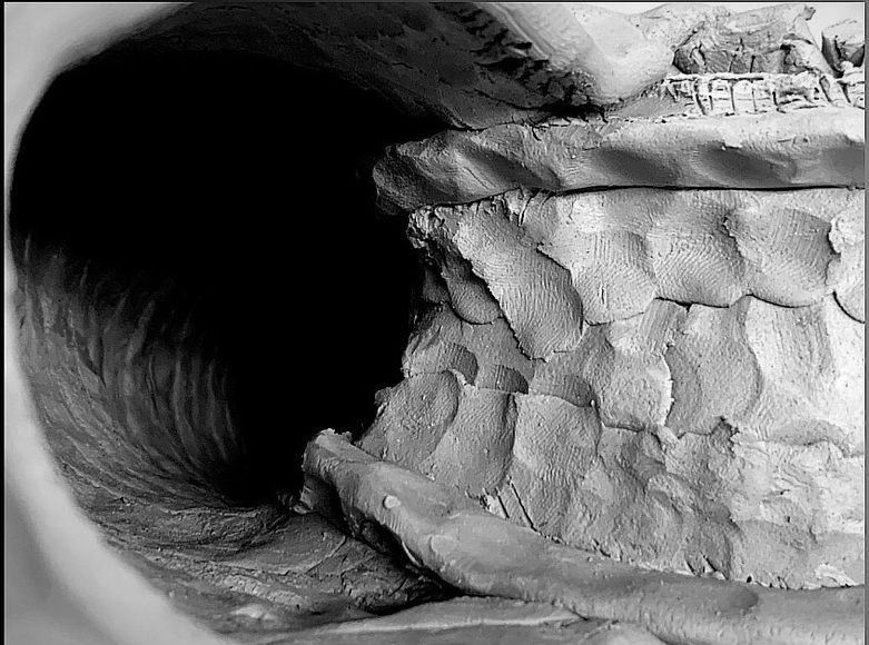 Black and white image looking down an unlit tunnel made by thumb-pressed clay.