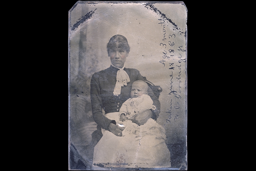 Tintype photograph of a Black woman sitting with a baby on her lap with text written directly on the right side of the photograph.