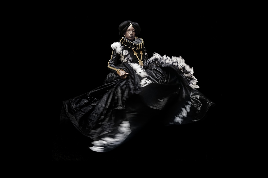 Photographic portrait of a Black woman in Elizabethan dress who appears to float against a black background with the ruffles of her dress in motion.