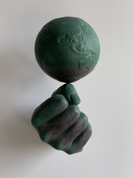 Ceramic wall sculpture of a clenched first balancing the world atop of its thumb.