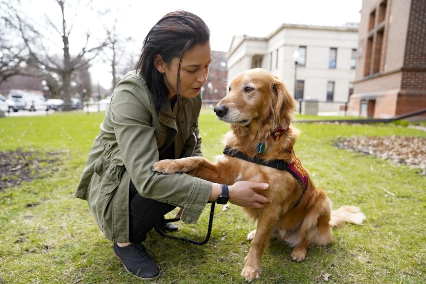 A woman squats next to Frankie the therapy dog outside Shevlin Hall. Frankie rests a paw on her arm.