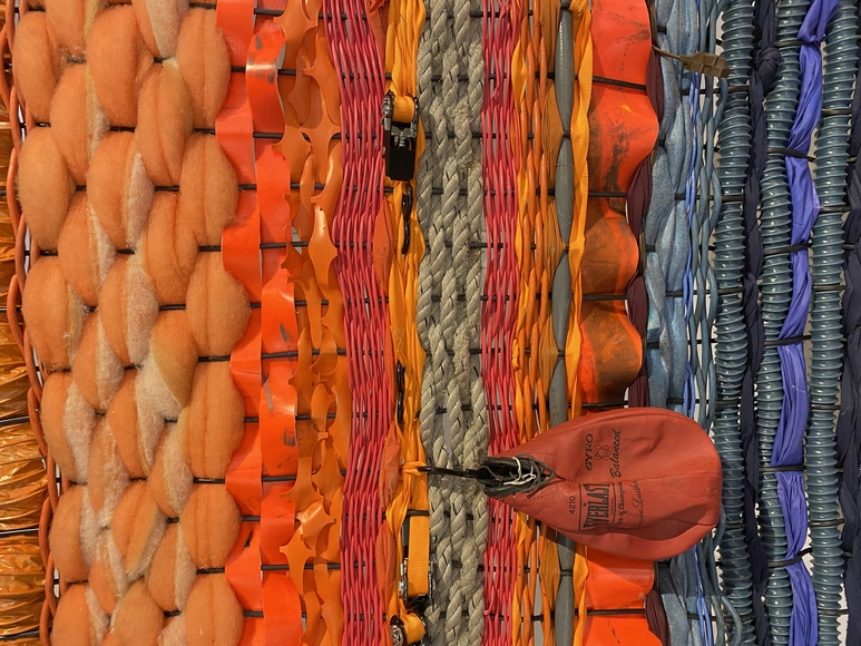 Close-up detail of woven sculpture made of orange and purple straps and rope