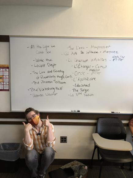 Image of a masked student giving a thumbs up in front of a white board.