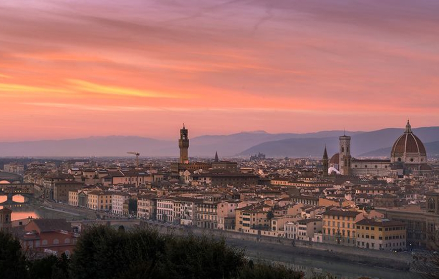 European cityscape under a pink and orange sunset with purple hills in the background