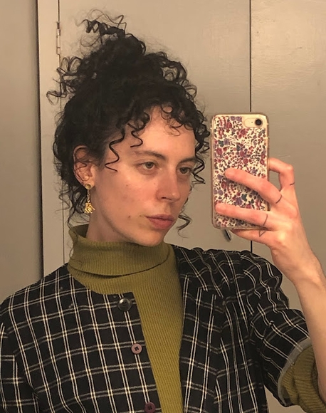 Alter Hajek takes a mirror selfie with a smartphone while wearing green turtleneck and plaid shirt